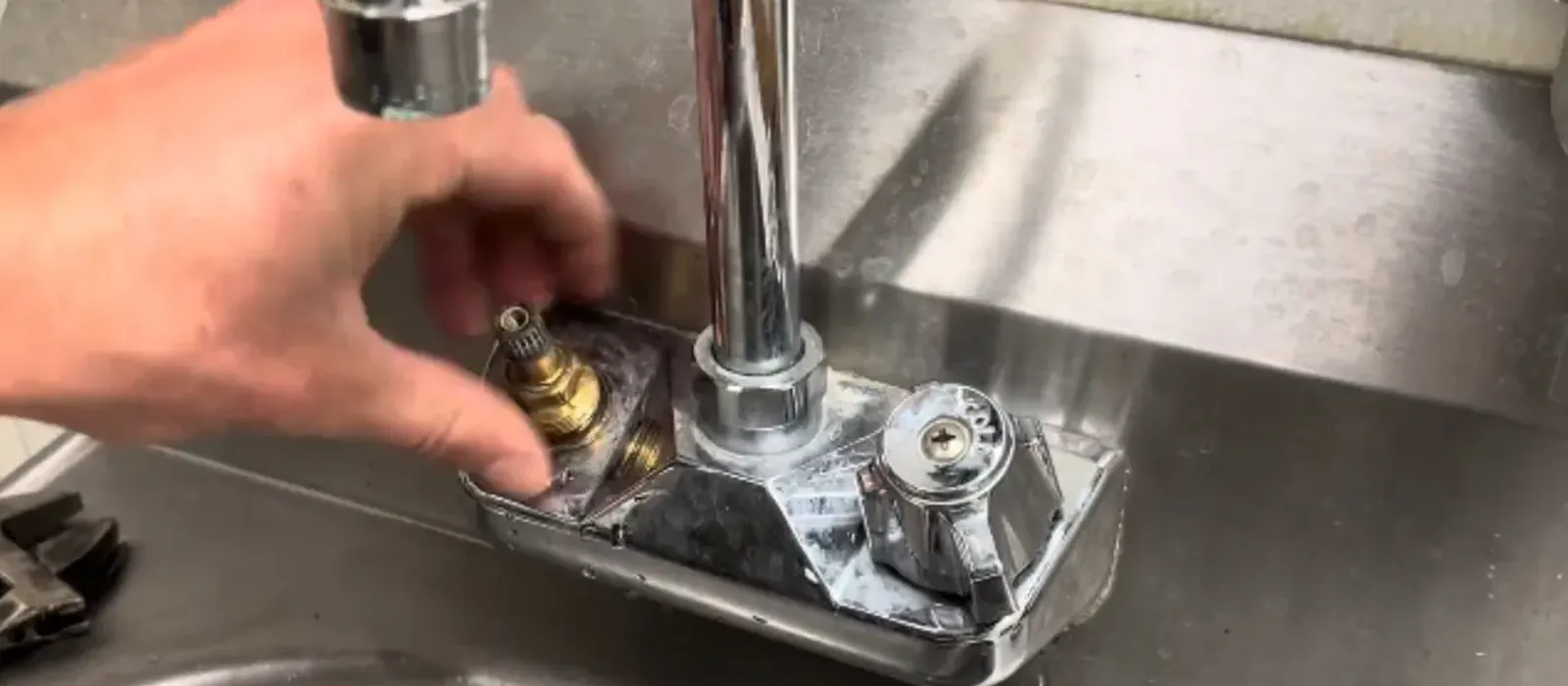 A hand removing the cartridge from a chrome two-handle faucet on a stainless steel sink