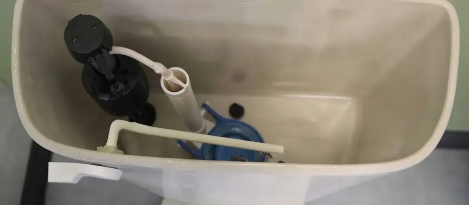 The inside of an open toilet tank showing the fill valve, flapper and overflow tube